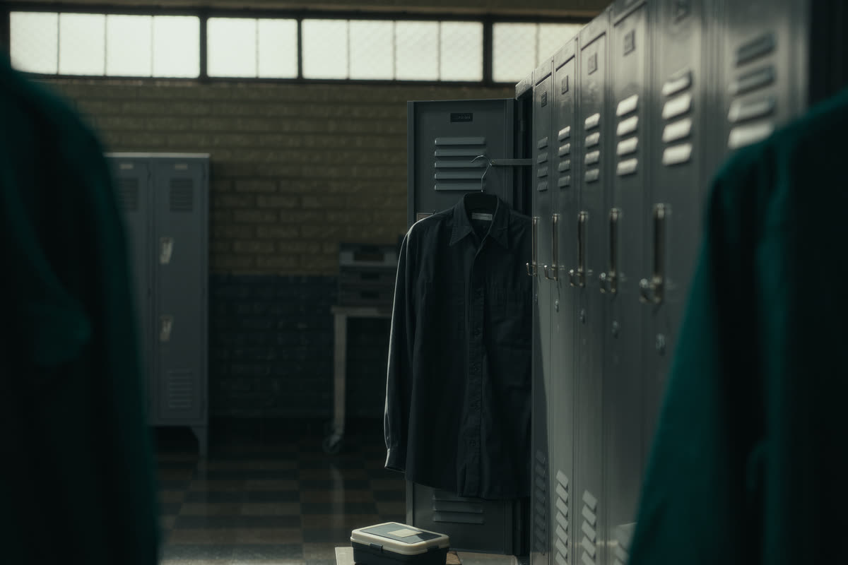 Camisa de uniforme pendurada num armário de vestiário, com uma marmita no banco